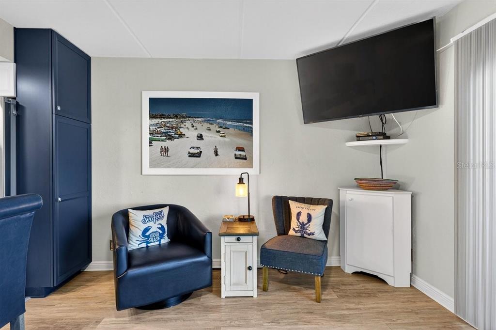 A living area features two blue chairs, a small side table, and a wall-mounted television — 2700 OCEAN SHORE BOULEVARD UNIT 106, ORMOND BEACH, FL