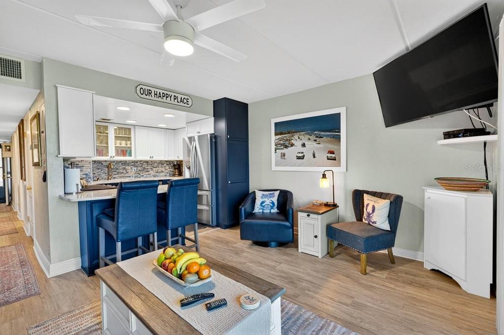 A living room and kitchen area with blue cabinetry, a ceiling fan, and coastal decor — 2700 OCEAN SHORE BOULEVARD UNIT 106, ORMOND BEACH, FL