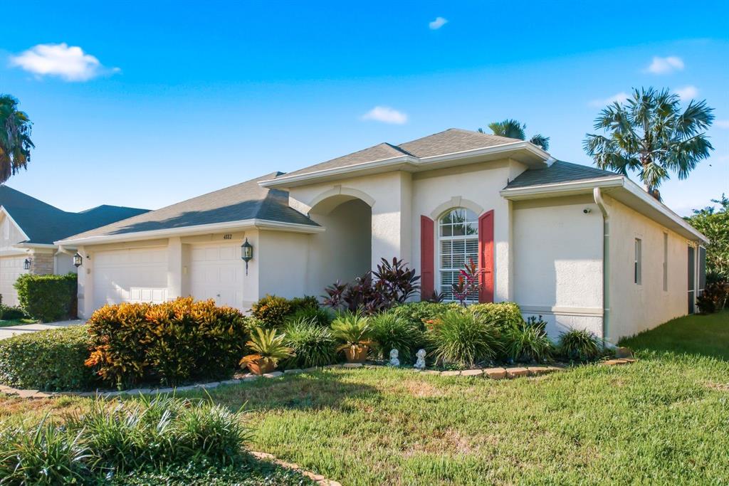 A single-story house with a two-car garage, beige stucco siding, and red window shutters — 4882 W BREEZE CIRCLE, PALM HARBOR, FL