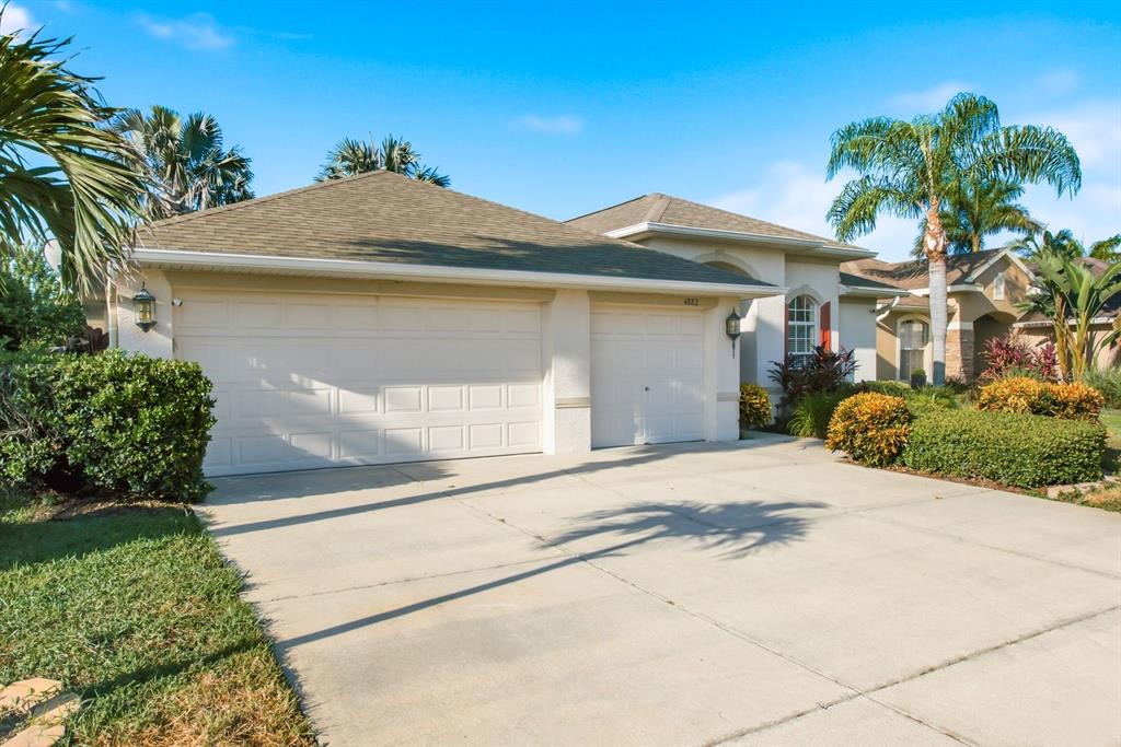 A beige house with a three-car garage and a concrete driveway under a blue sky — 4882 W BREEZE CIRCLE, PALM HARBOR, FL