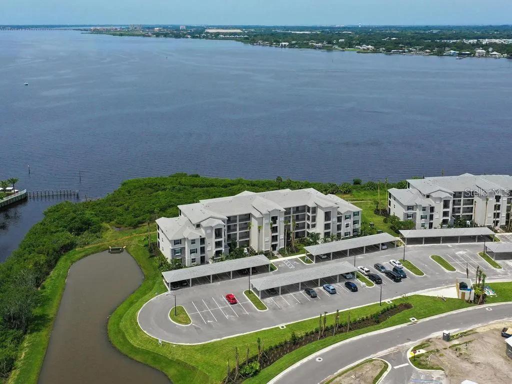An aerial view shows a multi-story apartment building with covered parking next to a river — 850 TIDEWATER SHORES LOOP UNIT 402, BRADENTON, FL