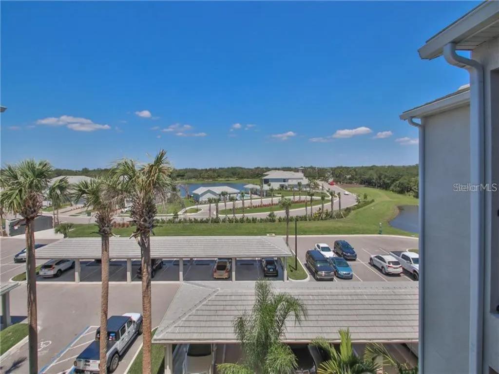 An elevated outdoor view shows a parking lot with covered spaces, palm trees, and a lake — 850 TIDEWATER SHORES LOOP UNIT 402, BRADENTON, FL