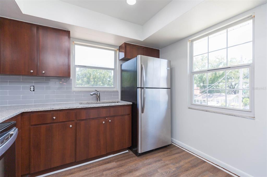 A kitchen features dark wood cabinets, granite countertops, a stainless steel refrigerator, and gray backsplash — 8510 N TAMPA STREET UNIT B, TAMPA, FL