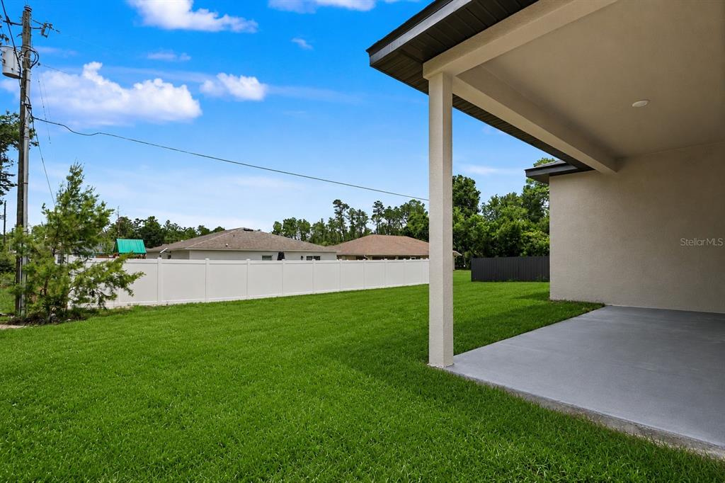 A view of a backyard with a green lawn, white vinyl fence, and covered patio — 4814 SW 166TH LOOP, OCALA, FL