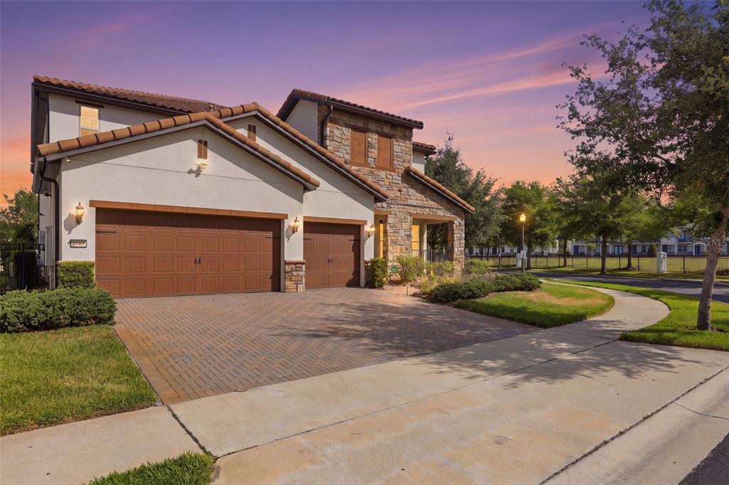 A two-story house with a three-car garage, stone accents, and a paved driveway at sunset — 10902 CITRON OAKS DRIVE, ORLANDO, FL