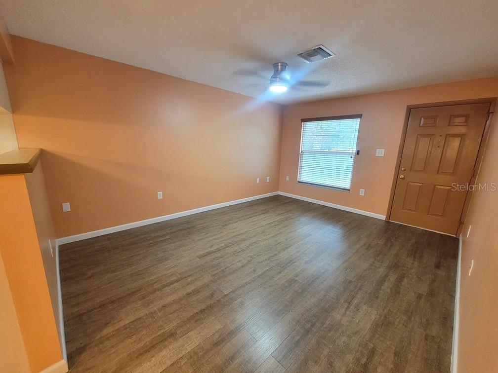 An empty room with light orange walls, wood-look flooring, a ceiling fan, and a door — 6141 CHESHAM DRIVE UNIT 8, NEW PORT RICHEY, FL