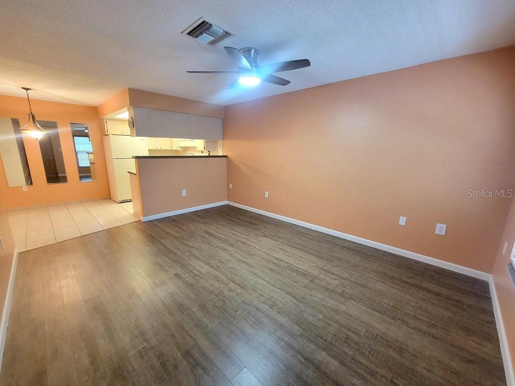 A living room with wood-look flooring and a ceiling fan opens to a kitchen area — 6141 CHESHAM DRIVE UNIT 8, NEW PORT RICHEY, FL