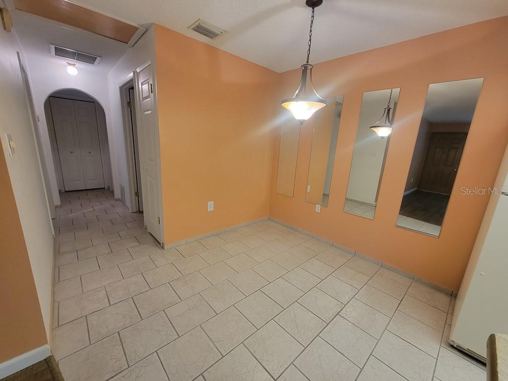 A dining area with peach walls, tiled flooring, a hanging light fixture, and wall mirrors — 6141 CHESHAM DRIVE UNIT 8, NEW PORT RICHEY, FL