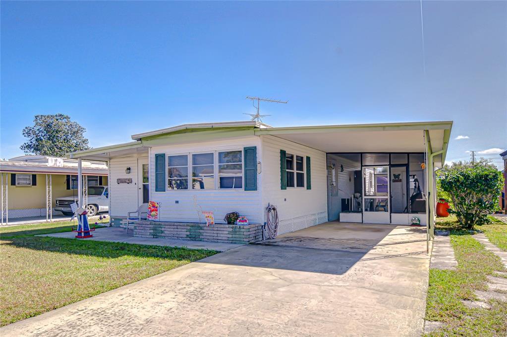 A single-story mobile home with white siding, blue shutters, a carport, and a concrete driveway — 35132 ZEPHYR SHORES DRIVE, ZEPHYRHILLS, FL