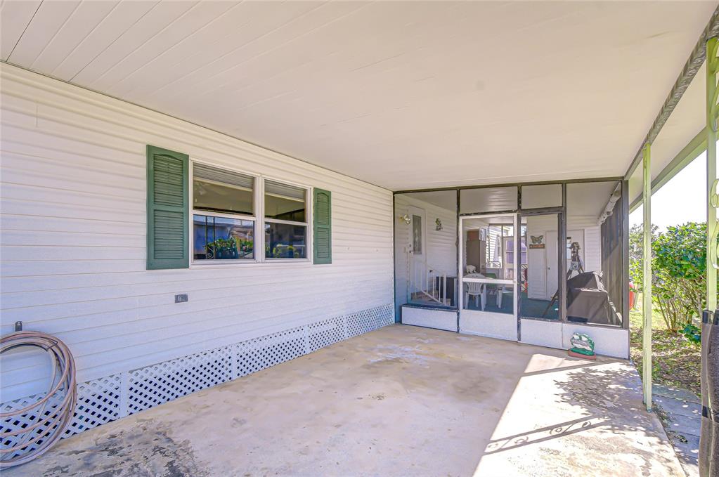 A covered concrete patio features white siding, green shutters, and a screened-in porch area — 35132 ZEPHYR SHORES DRIVE, ZEPHYRHILLS, FL