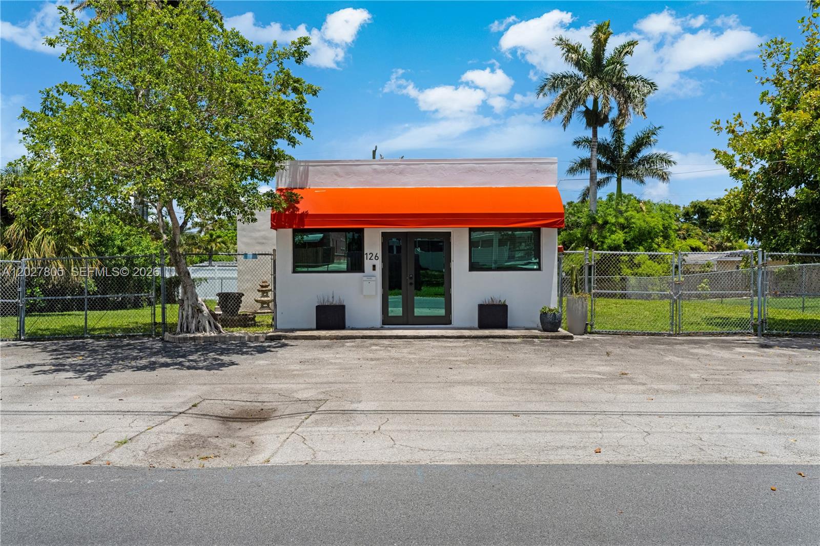 A small white commercial building features an orange awning, glass double doors, and a chain-link fence — 126 NE 1st Ave, Dania Beach FL 33004, DANIA BEACH, FL
