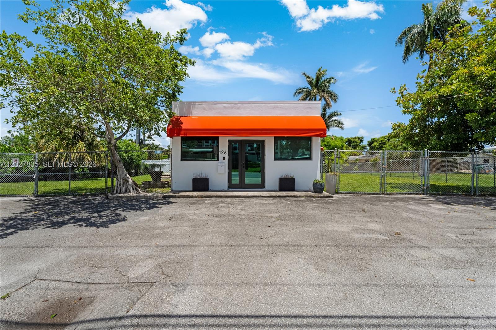 A small, white, single-story commercial building features an orange awning and a paved parking lot — 126 NE 1st Ave, Dania Beach FL 33004, DANIA BEACH, FL