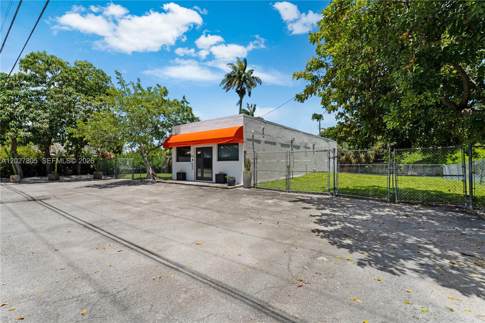 A small, white commercial building features an orange awning and a fenced-in grassy lot — 126 NE 1st Ave, Dania Beach FL 33004, DANIA BEACH, FL