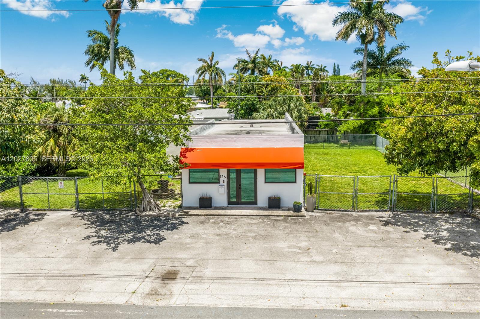 A small, white, flat-roofed commercial building features an orange awning and a fenced yard — 126 NE 1st Ave, Dania Beach FL 33004, DANIA BEACH, FL