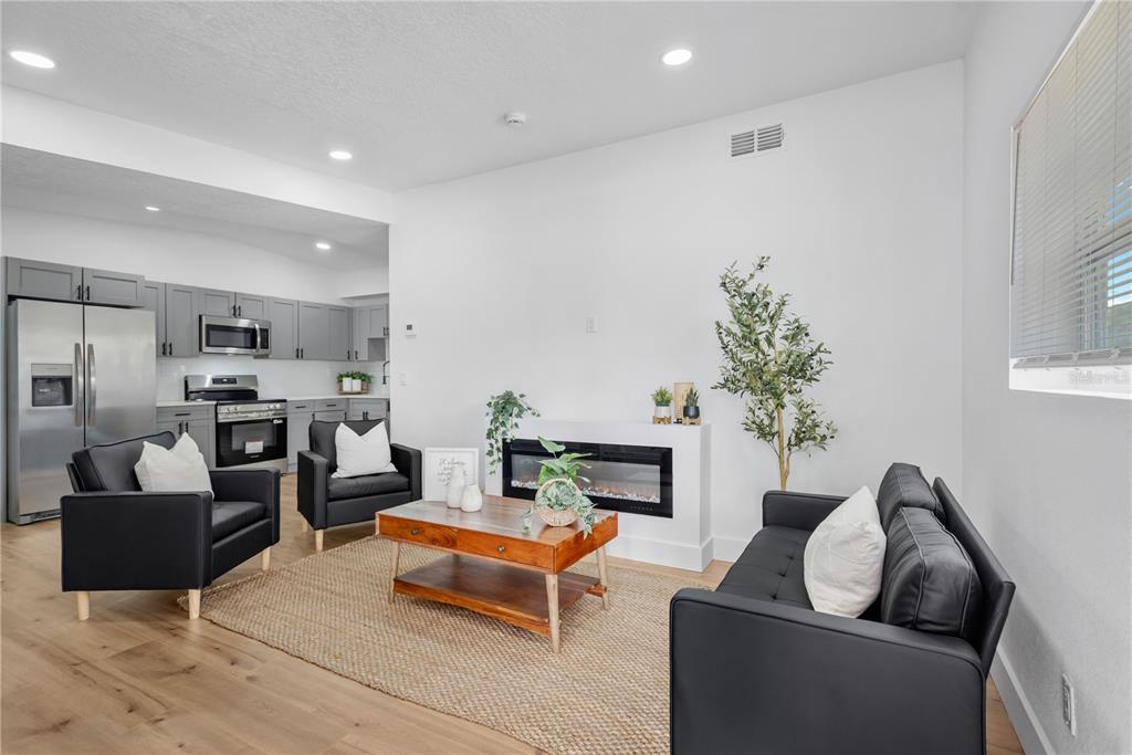 A living room with a fireplace and black furniture opens into a kitchen with gray cabinets — 4628 15TH AVENUE S, ST PETERSBURG, FL
