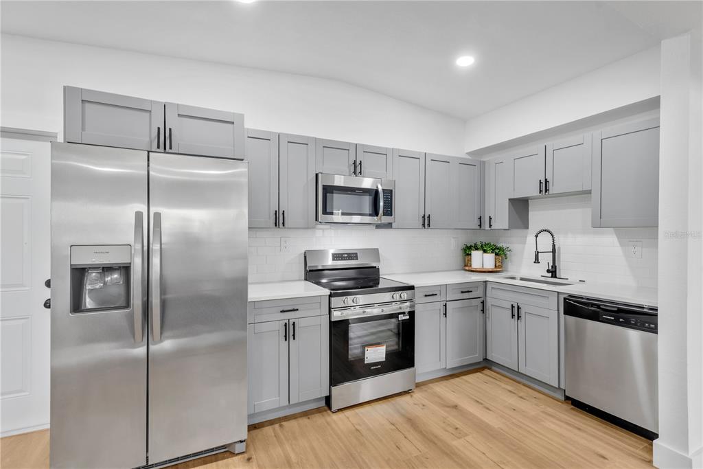 A kitchen features light gray cabinets, stainless steel appliances, white countertops, and wood-look flooring — 4628 15TH AVENUE S, ST PETERSBURG, FL