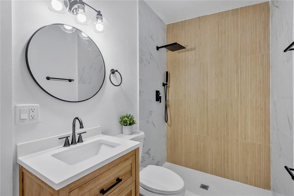 A modern bathroom features a vanity with a round mirror, a toilet, and a tiled shower — 4628 15TH AVENUE S, ST PETERSBURG, FL