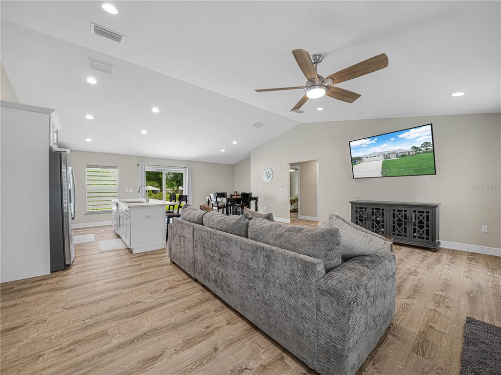 A living room with a gray sectional sofa, wood-look flooring, and an open-concept kitchen — 270 LINCOLN ROAD NE, LAKE PLACID, FL