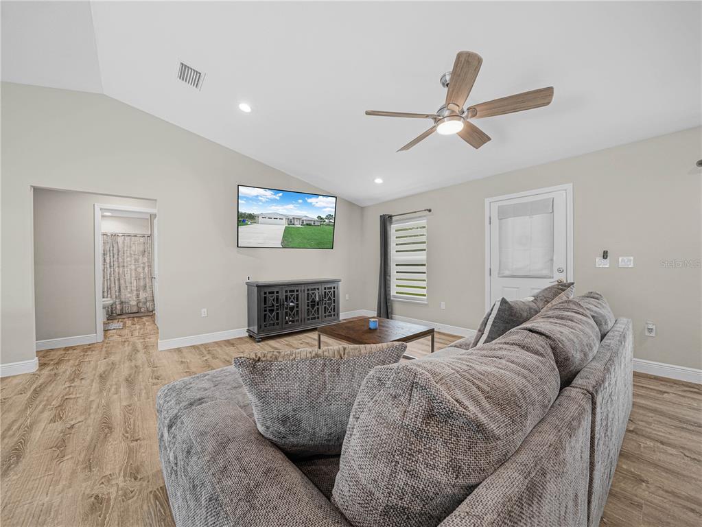 A living room features a vaulted ceiling, wood-look flooring, a gray sectional, and a television — 270 LINCOLN ROAD NE, LAKE PLACID, FL