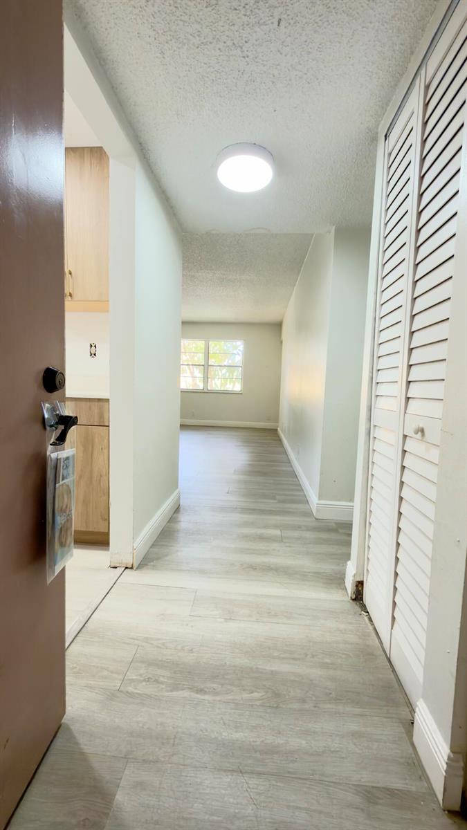 A hallway with light wood-look flooring leads to a living area with a window — 4364 NW 9th # 2a, Deerfield Beach FL 33064, DEERFIELD BEACH, FL