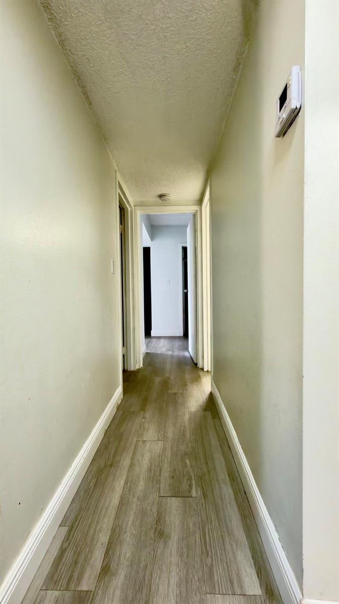 A narrow hallway features light-colored walls, wood-look flooring, and a textured ceiling — 4364 NW 9th # 2a, Deerfield Beach FL 33064, DEERFIELD BEACH, FL