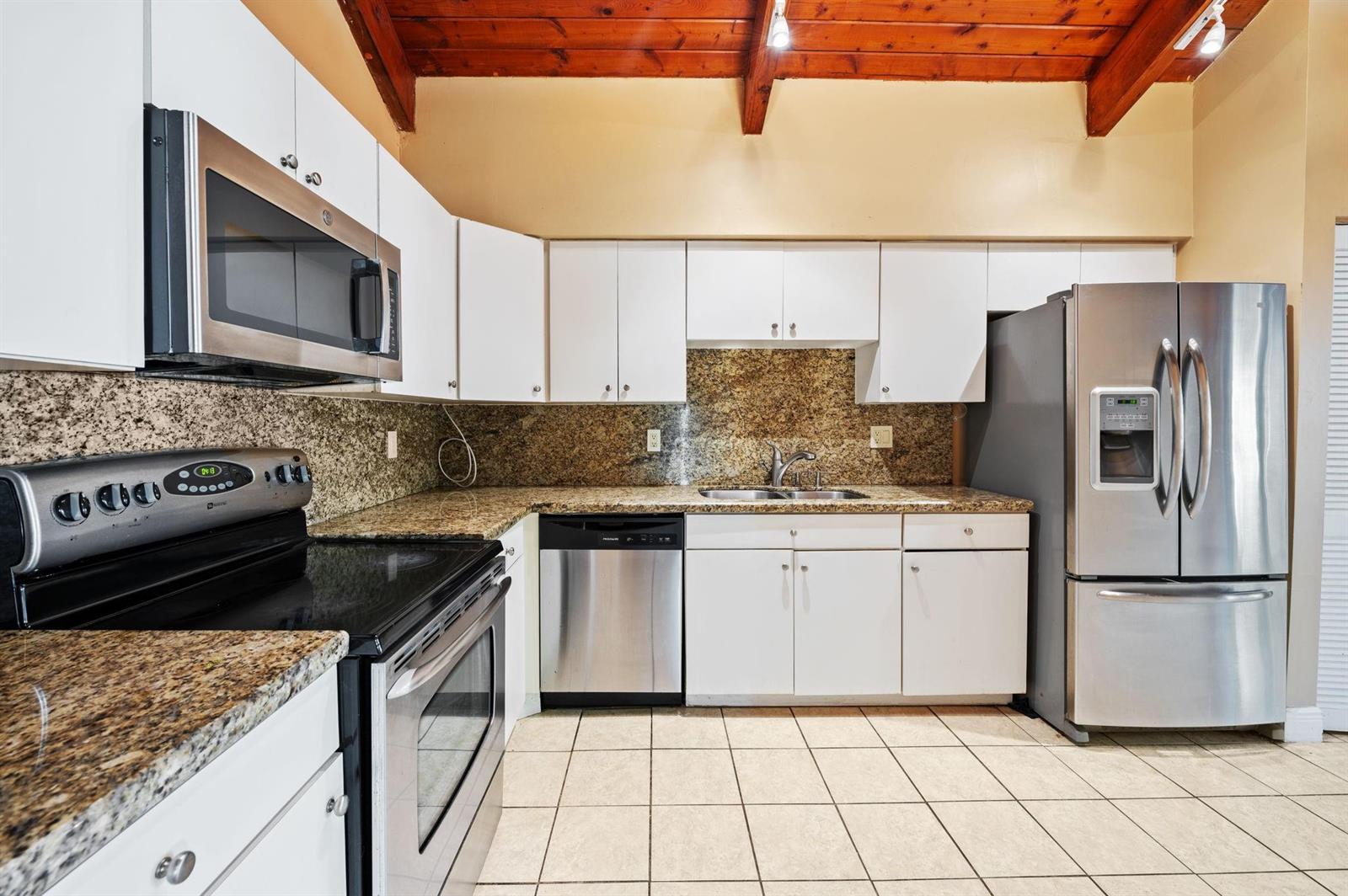 A kitchen features white cabinets, granite countertops, stainless steel appliances, and a wood-beamed ceiling — 2229 Nova Village Drive, Davie FL 33317, DAVIE, FL