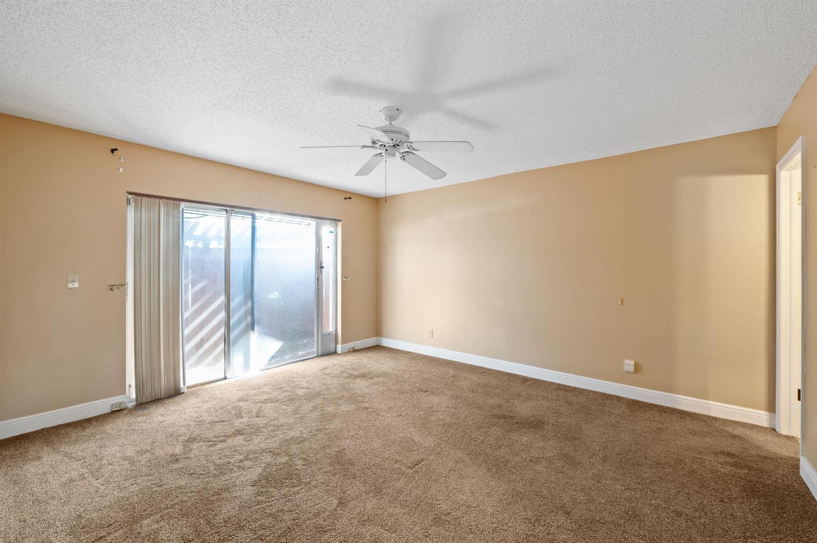 An empty bedroom features beige walls, brown carpeting, a ceiling fan, and sliding glass doors — 2229 Nova Village Drive, Davie FL 33317, DAVIE, FL