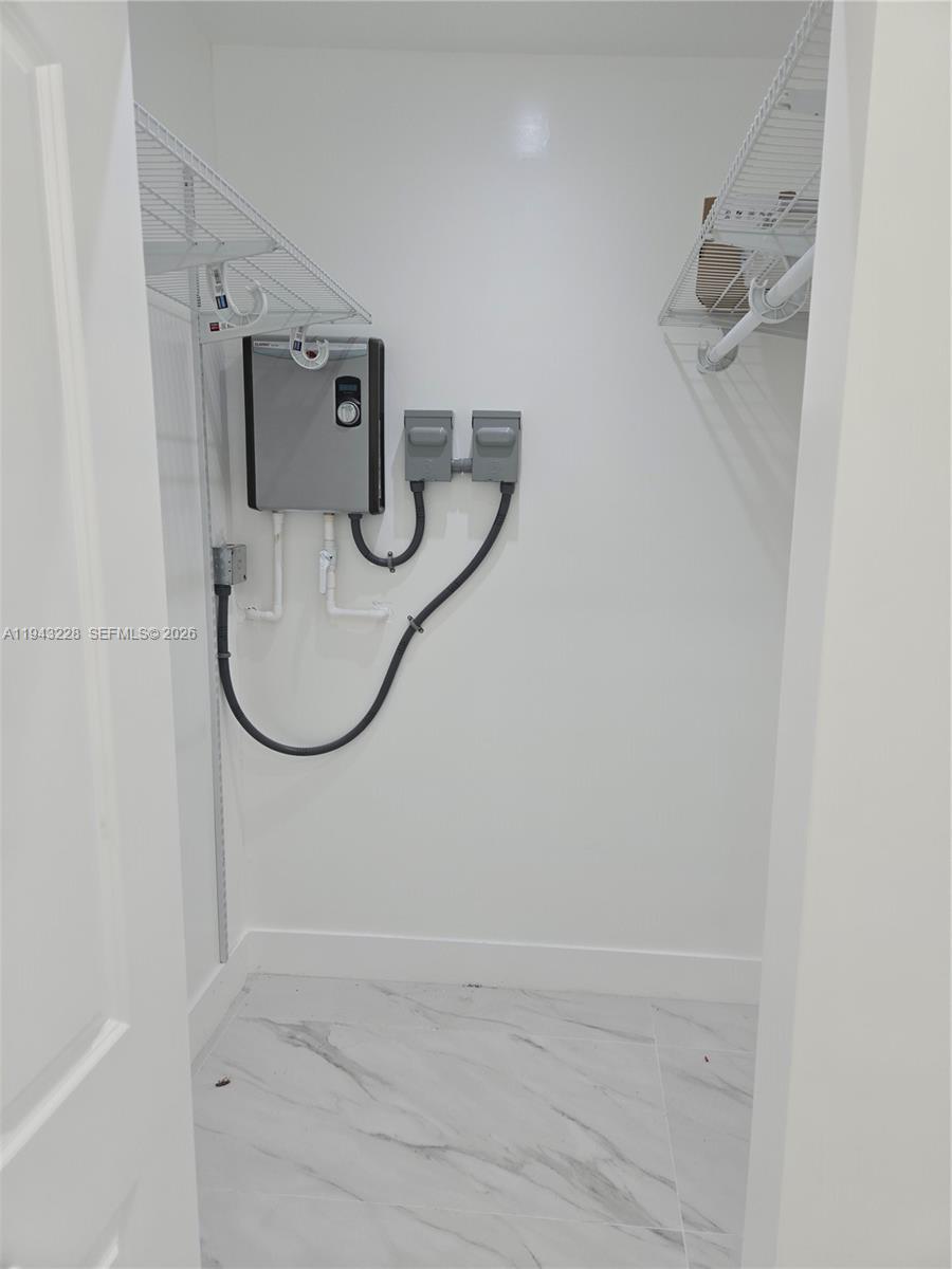 A small utility closet features a tankless water heater, electrical disconnects, and wire shelving — 987 NE 145 # B, North Miami FL 33161, NORTH MIAMI, FL