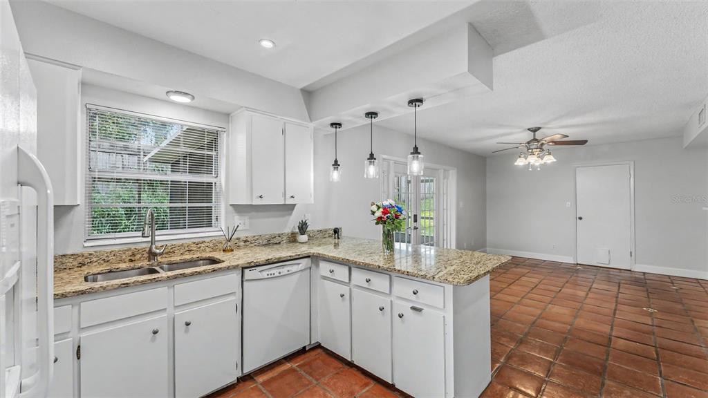 A kitchen with white cabinets, granite countertops, and tile flooring opens to a dining area — 1218 LAKE ARIANA BOULEVARD, AUBURNDALE, FL