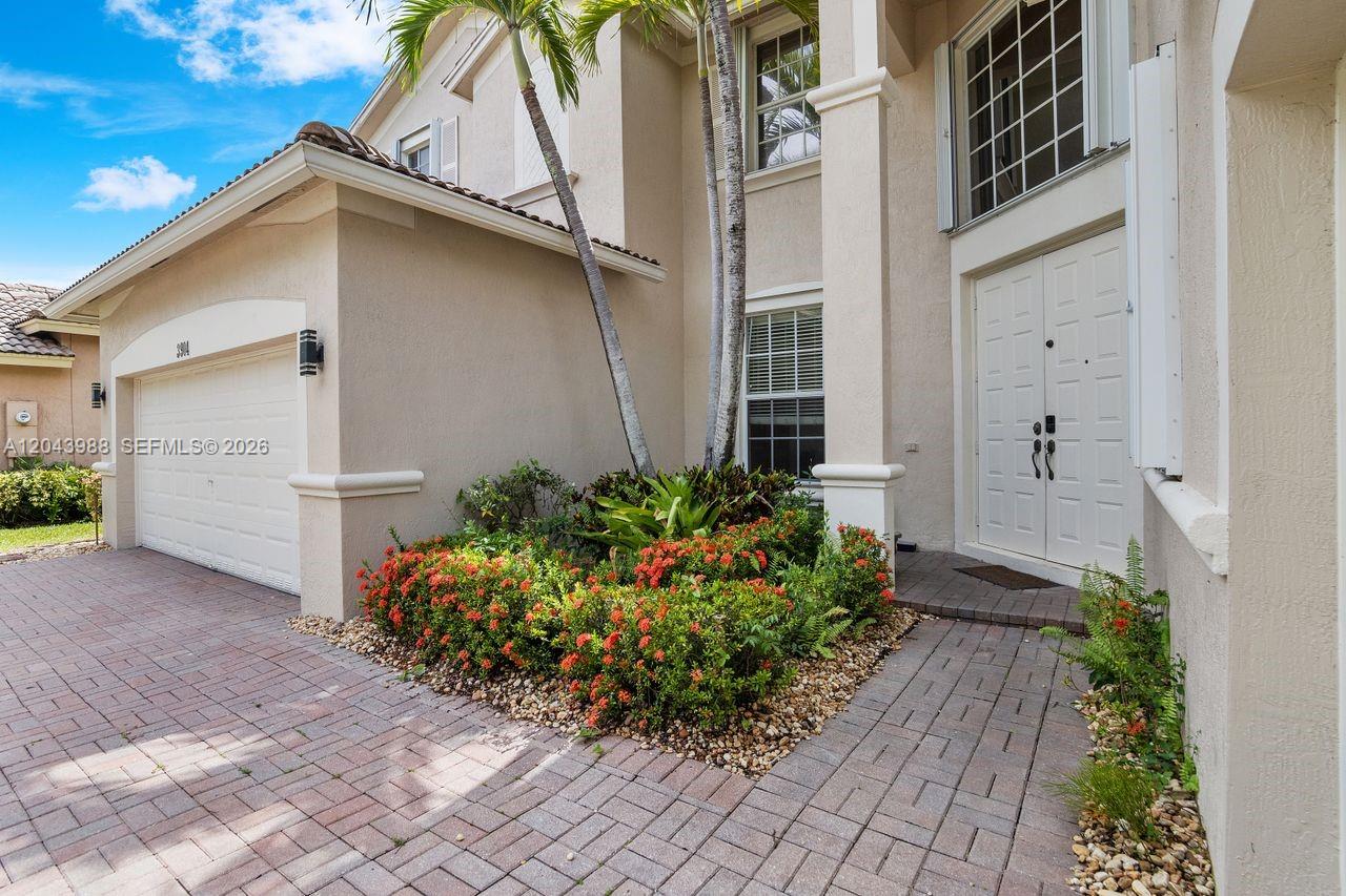 A beige two-story house features a garage, a brick driveway, and a landscaped front entrance — 3904 W Gardenia Ave, Weston FL 33332, WESTON, FL