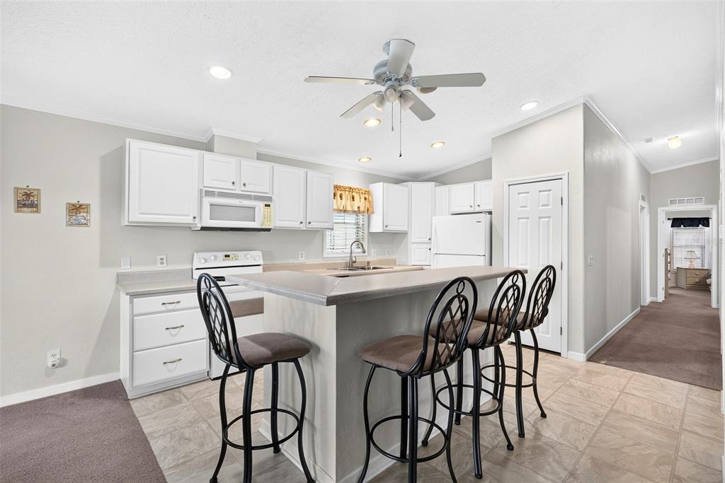 A kitchen features white cabinets, a breakfast bar with three stools, and tile flooring — 15550 BURNT STORE ROAD UNIT 237, PUNTA GORDA, FL