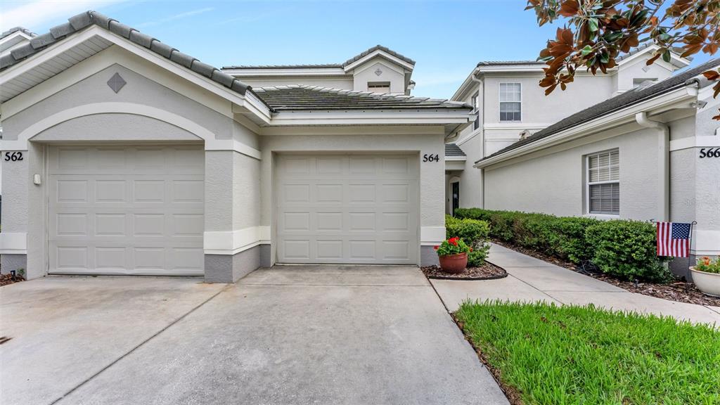 The exterior of a multi-unit residential building features two garage doors and a walkway — 564 GRASSLANDS VILLAGE CIRCLE, LAKELAND, FL