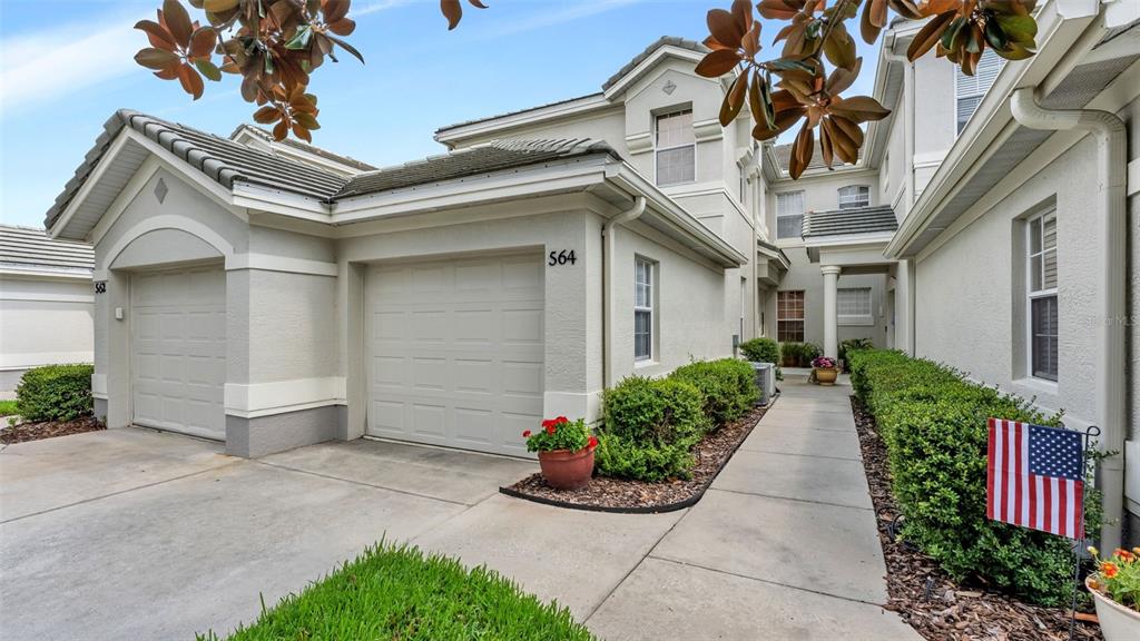A two-story townhouse exterior features a two-car garage, a walkway, and manicured landscaping — 564 GRASSLANDS VILLAGE CIRCLE, LAKELAND, FL