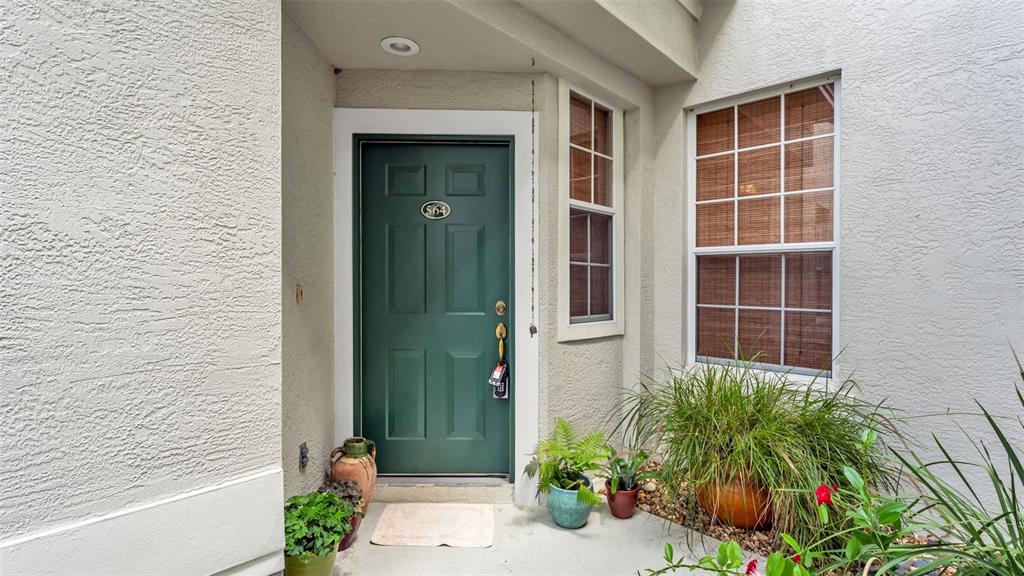 A green front door with a number plate sits beside a window and potted plants — 564 GRASSLANDS VILLAGE CIRCLE, LAKELAND, FL