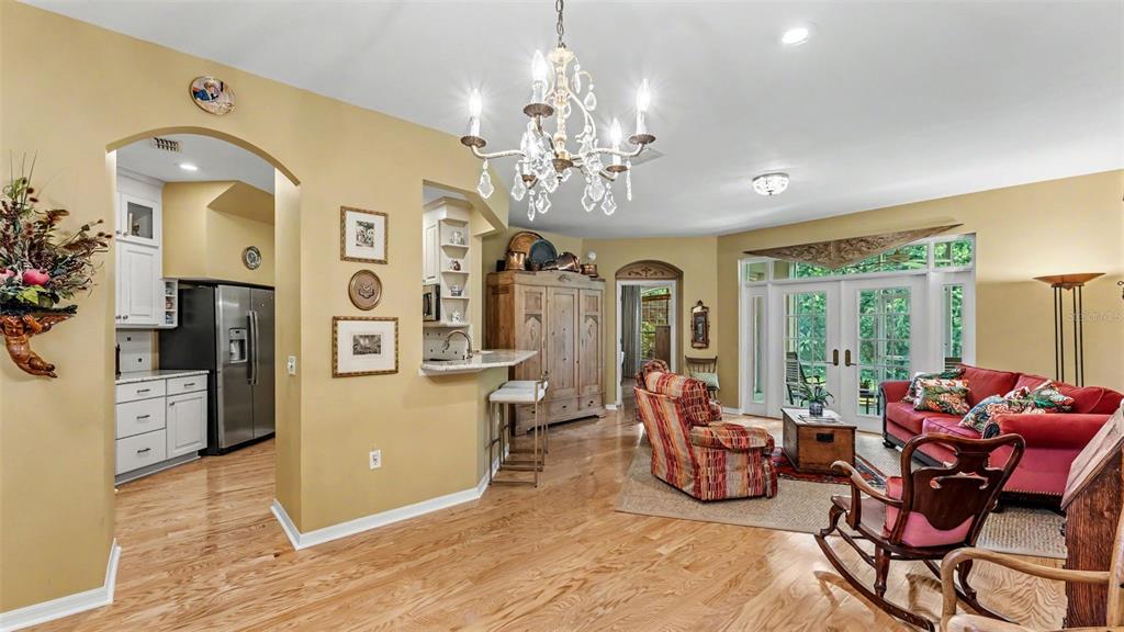 A living room with a chandelier, hardwood floors, and a red sofa near glass doors — 564 GRASSLANDS VILLAGE CIRCLE, LAKELAND, FL