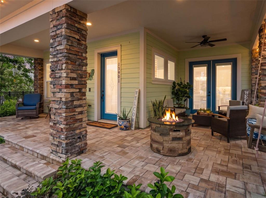 A covered patio features stone columns, a fire pit, outdoor seating, and a blue front door — 13901 MYERSON AVENUE, ORLANDO, FL