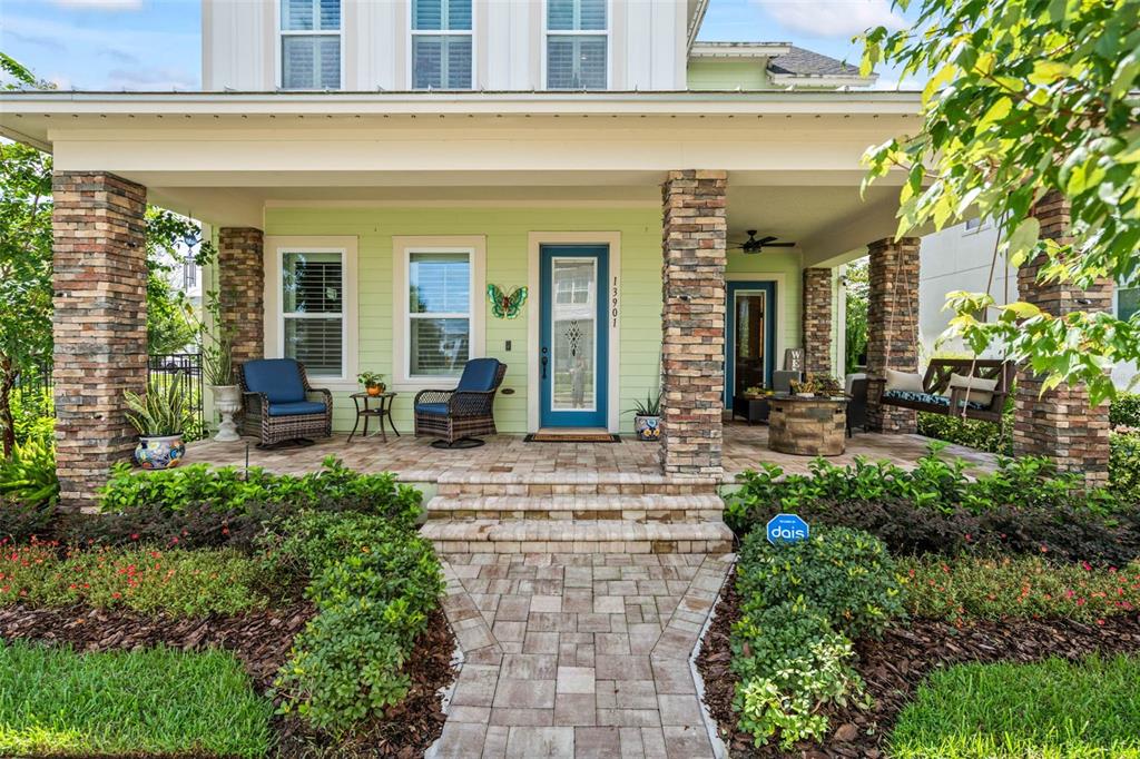 A light green house features a stone-pillared front porch with a blue door and furniture — 13901 MYERSON AVENUE, ORLANDO, FL
