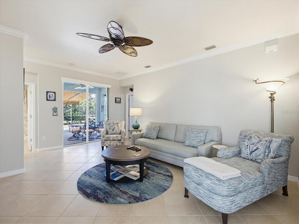 A living room features a sofa, patterned armchairs, a round coffee table, and sliding glass doors — 11697 SPOTTED MARGAY AVENUE, VENICE, FL