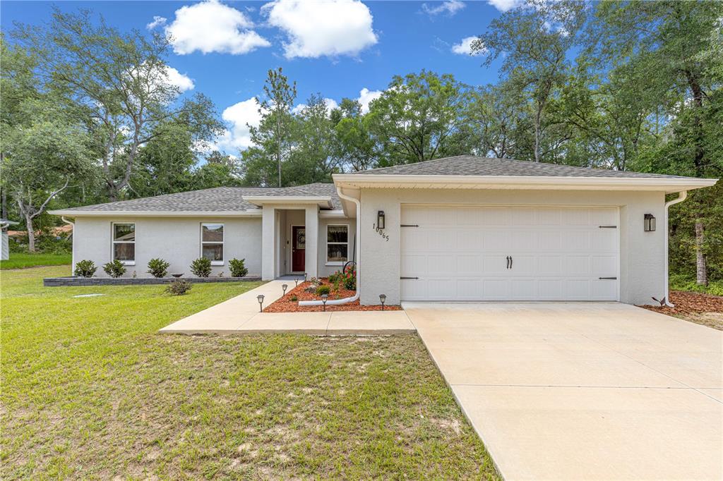 A single-story house with a white stucco exterior, a two-car garage, and a landscaped yard — 10065 N LANGDON ROAD, CITRUS SPRINGS, FL