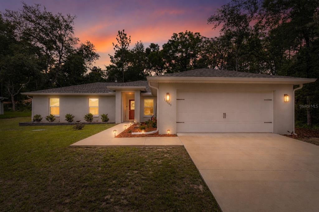A single-story house with a white stucco exterior, a two-car garage, and a sunset sky — 10065 N LANGDON ROAD, CITRUS SPRINGS, FL