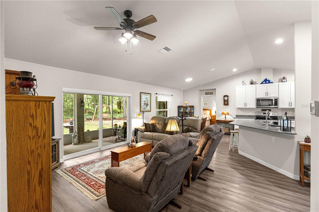 An open-concept living room and kitchen with wood-look flooring, vaulted ceilings, and a sliding door — 10065 N LANGDON ROAD, CITRUS SPRINGS, FL