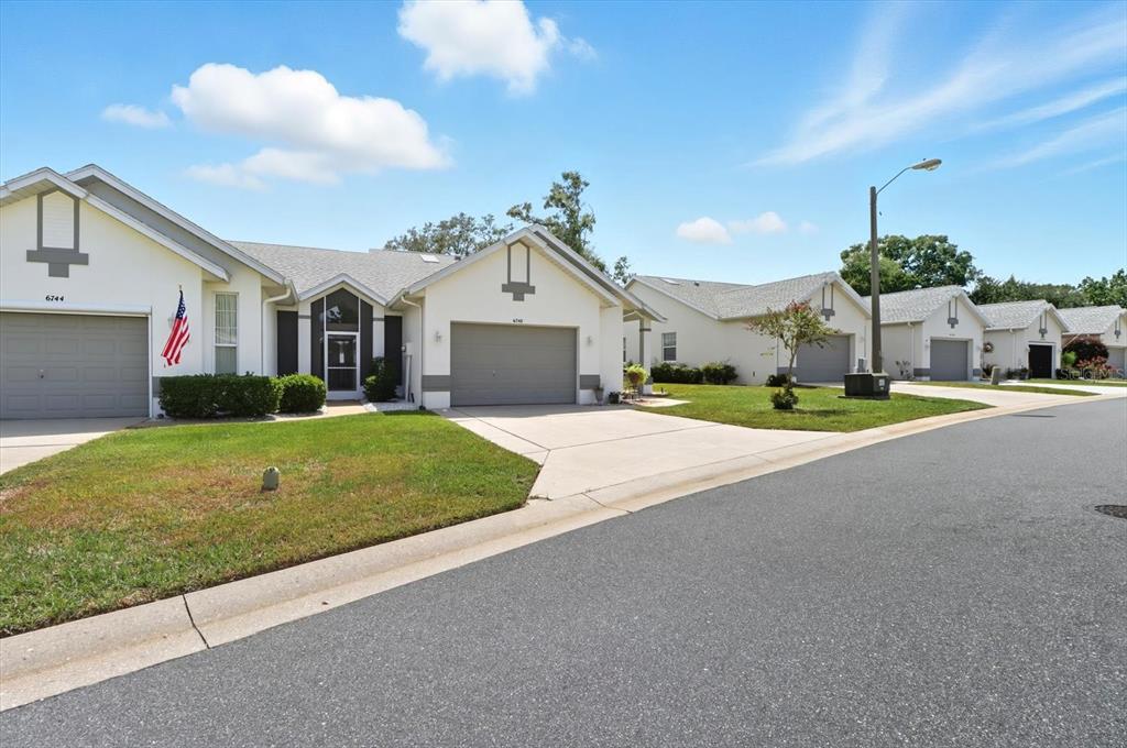 A row of single-story suburban houses with attached garages and driveways under a blue sky — 6740 E KINGSBURY LANE, INVERNESS, FL