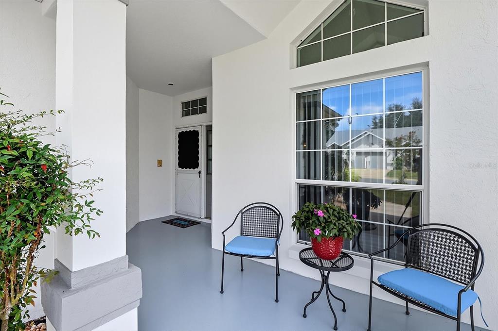 A covered front porch features a gray floor, two chairs, a small table, and windows — 6740 E KINGSBURY LANE, INVERNESS, FL