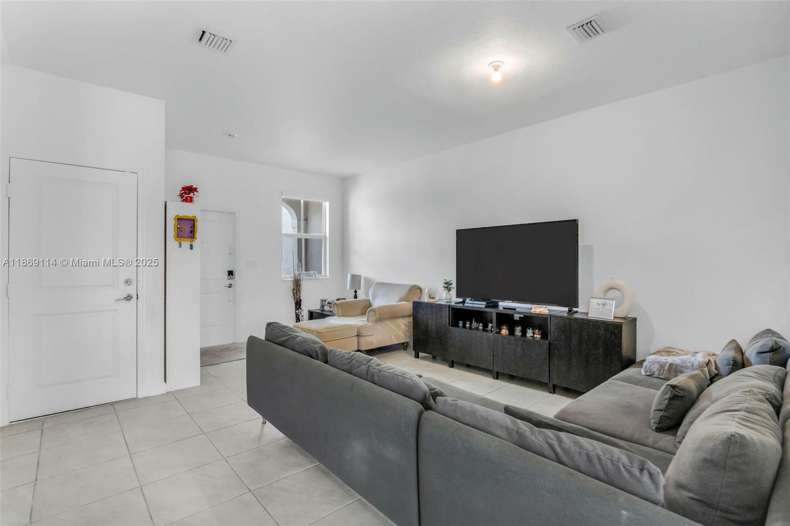 A living room features a gray sectional sofa, a television on a stand, and tile flooring — 12774 NW 22nd Pl, Miami FL 33167, MIAMI, FL