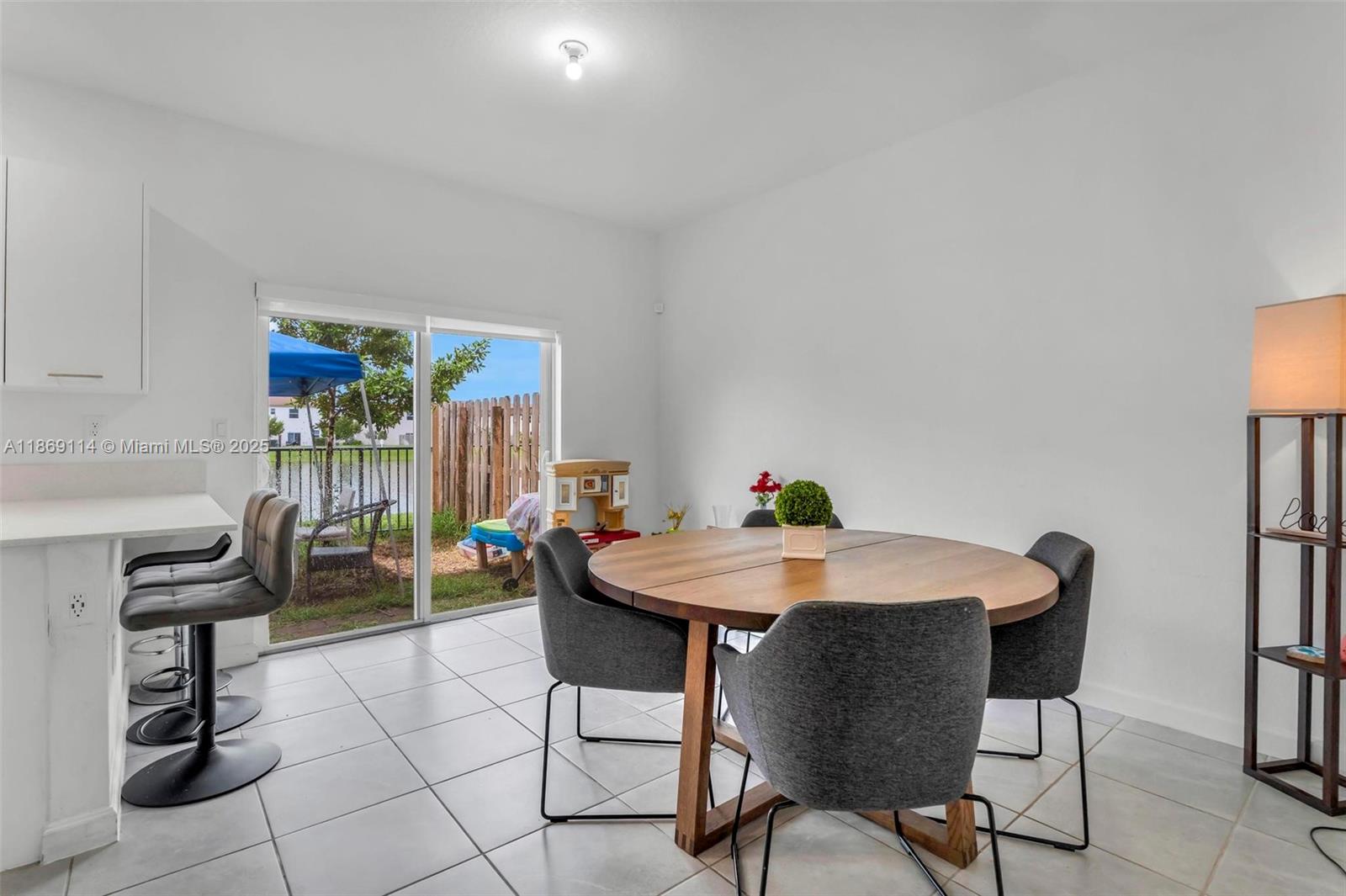 A dining area features a round wooden table, gray chairs, tile floors, and sliding doors — 12774 NW 22nd Pl, Miami FL 33167, MIAMI, FL