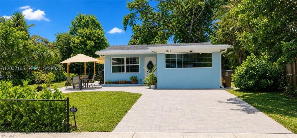 A light blue single-story house features a paved driveway, a patio with an umbrella, and landscaping — FORT MYERS, FL