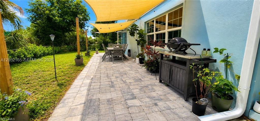 A paved patio features a dining set, a grill station, and shade sails along a house — FORT MYERS, FL