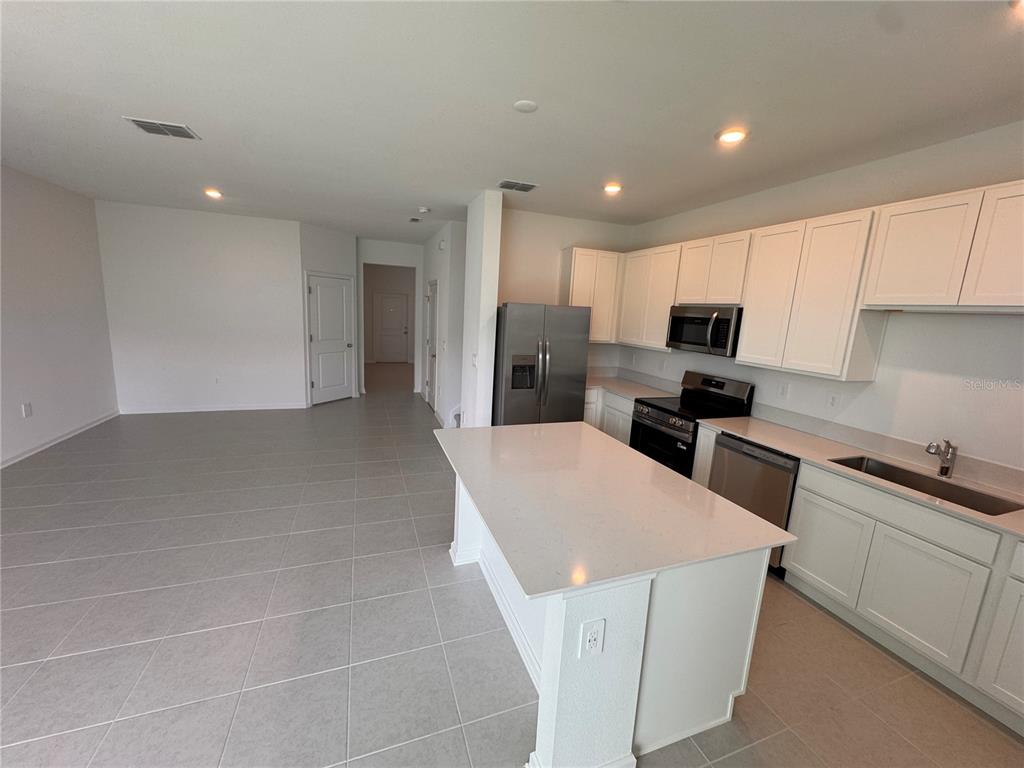 A kitchen features white cabinetry, stainless steel appliances, a quartz island, and light tile flooring — 3135 MINDFULLNESS DRIVE, CLERMONT, FL