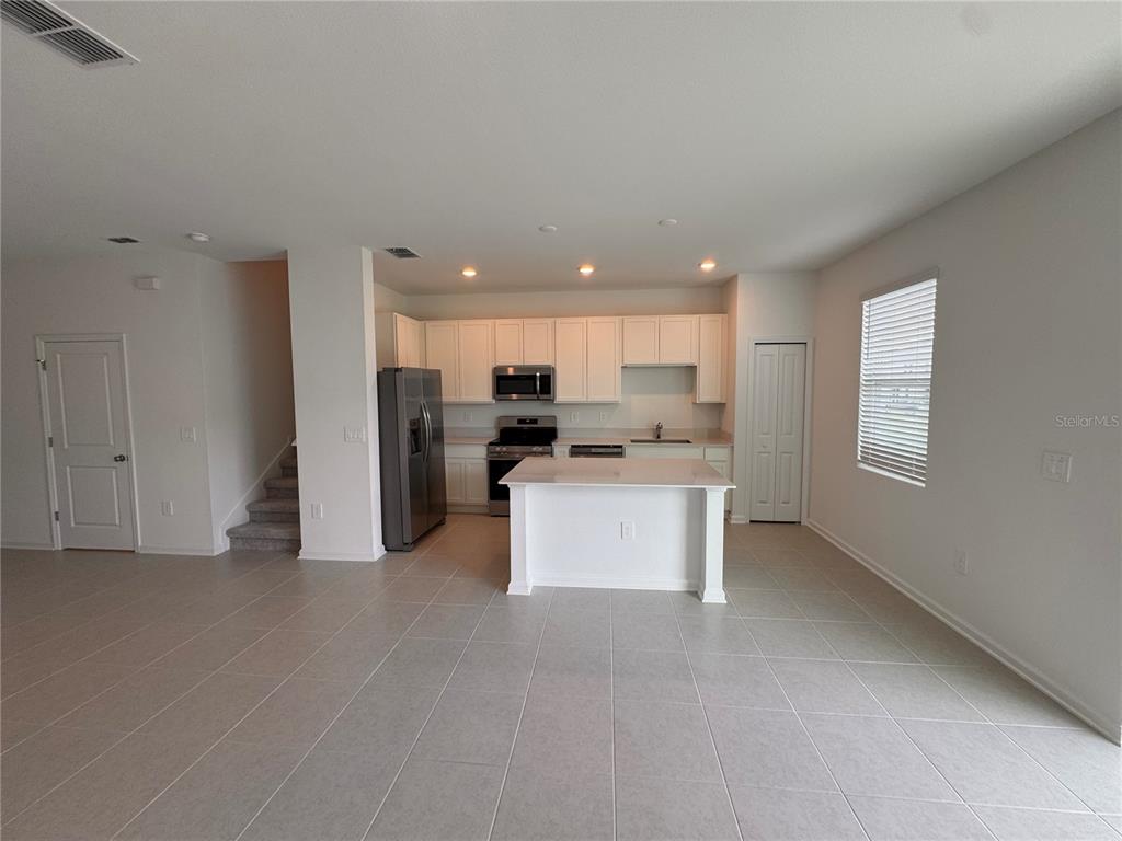 A kitchen with white cabinets, stainless steel appliances, and an island sits in an open-concept room — 3135 MINDFULLNESS DRIVE, CLERMONT, FL