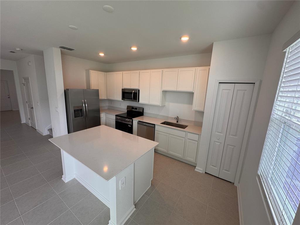 A kitchen features white cabinetry, stainless steel appliances, a center island, and tiled flooring — 3135 MINDFULLNESS DRIVE, CLERMONT, FL